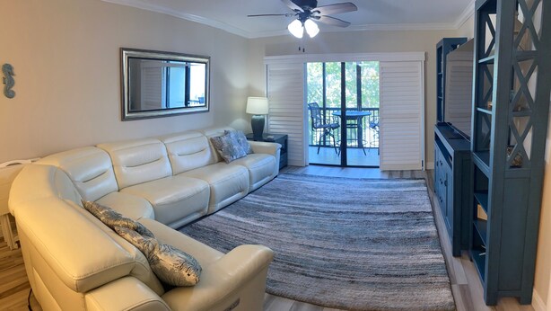 A living room with a beige sectional sofa, a ceiling fan, a large mirror, and a view to an outdoor patio. - Recently renovated third floor (Sarasota)
