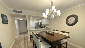A dining area with a wooden table and chairs, a chandelier, and a clock on the wall. - Recently renovated third floor (Sarasota)