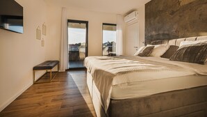A bedroom with a large bed, a bench, a TV mounted on the wall, and a view through a glass door. - Beautiful Villa Angelina in Kastelir (Kastelir)