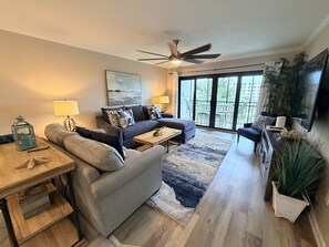A modern living room with a sofa, coffee table, and a dining table with a lantern. - Coastal comfort,3rd floor unit (Sarasota)