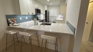 Cozinha moderna com armários brancos, geladeira de aço inoxidável e um espaço com banquetas.