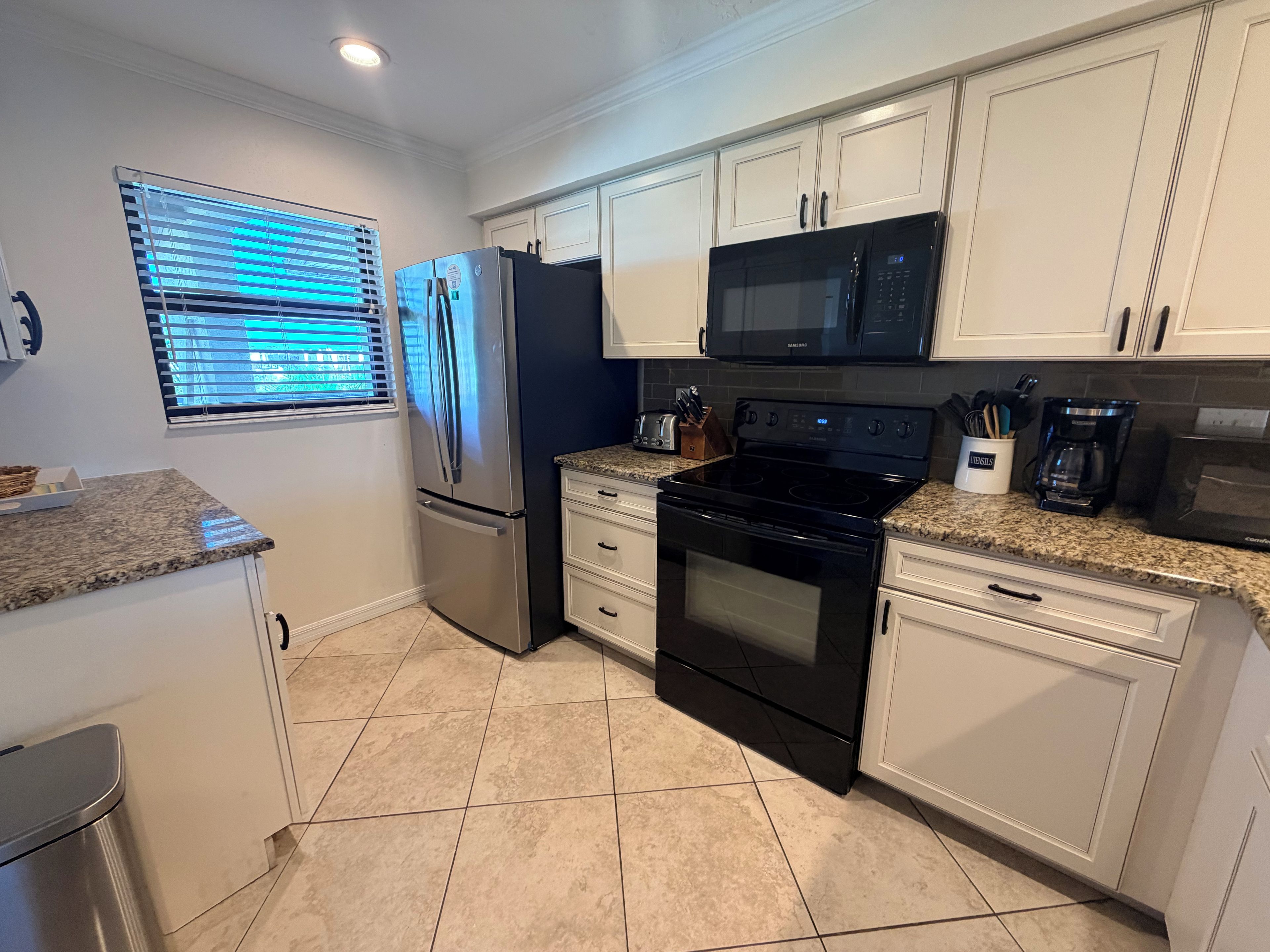 A modern kitchen with white cabinets, stainless steel appliances, and a tiled floor.