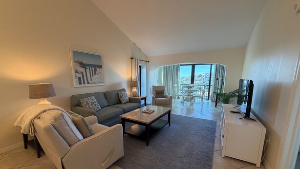 A modern living room with a sofa, armchair, coffee table, and a TV. There is a balcony with a view of the city. - Bright and spacious 3 bedroom, 4th Floor unit (Sarasota)