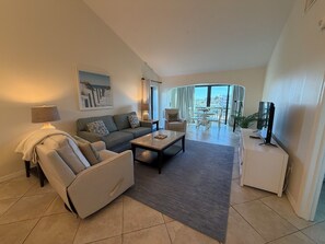 A modern living room with a sofa, armchair, coffee table, and a TV. There is a balcony with a view of the city. - Bright and spacious 3 bedroom, 4th Floor unit (Sarasota)