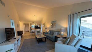 A spacious living room with a sofa, armchairs, a coffee table, and a TV. There is a dining area in the background with a kitchen visible. - Bright and spacious 3 bedroom, 4th Floor unit (Sarasota)