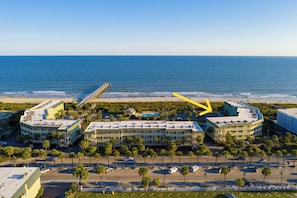 A coastal hotel with a beachfront view, multiple parking lots, and a prominent pier extending into the ocean.