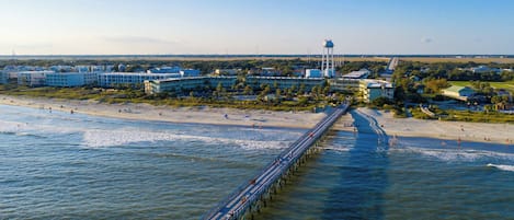 A coastal area with a long pier extending into the water, a beach, and buildings in the background.