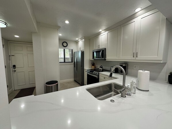 A modern kitchen with white cabinets, stainless steel appliances, and a marble countertop.