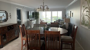 A dining area with a round table, wooden chairs, a chandelier, and a view of the outdoors. - Beautiful Beachfront 1st Floor condo (Sarasota)