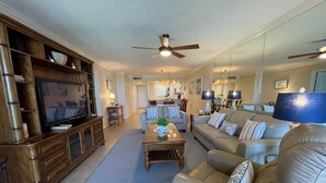 A spacious living room with a large flat-screen TV, leather sofas, a coffee table, and a ceiling fan. - Beachfront  2 bed/ 2 Bath Condo (Sarasota)