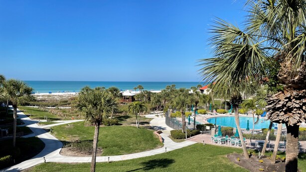 A resort with a swimming pool, palm trees, and a beach view. - Beachfront  2 bed/ 2 Bath Condo (Sarasota)