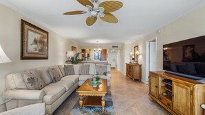 A living room with a beige sofa, a wooden coffee table, and a ceiling fan. - Spacious and Bright Gulf front 2 bed/2 bath condo (Sarasota)