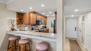 A kitchen with wooden cabinets, a granite countertop, and three bar stools. - Spacious and Bright Gulf front 2 bed/2 bath condo (Sarasota)