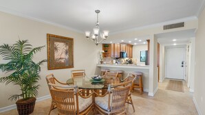 A dining area with a glass table surrounded by wicker chairs, a chandelier, a potted plant, and a framed picture on the wall. - Spacious and Bright Gulf front 2 bed/2 bath condo (Sarasota)