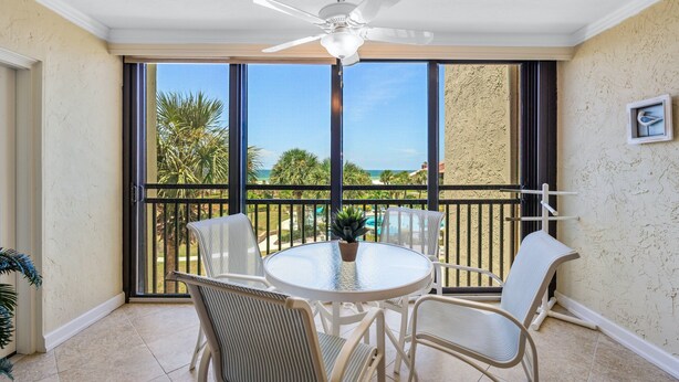 A balcony with a round table and chairs, a ceiling fan, and a view of the ocean and palm trees. - Spacious and Bright Gulf front 2 bed/2 bath condo (Sarasota)