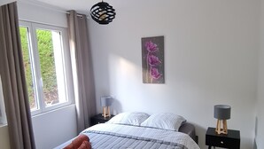 Un dormitorio con cama, dos mesitas de noche, una lámpara colgante, una ventana con cortinas y una obra de arte en la pared.