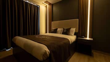 A modern bedroom with a large bed, dark curtains, and a bedside table with a lamp.