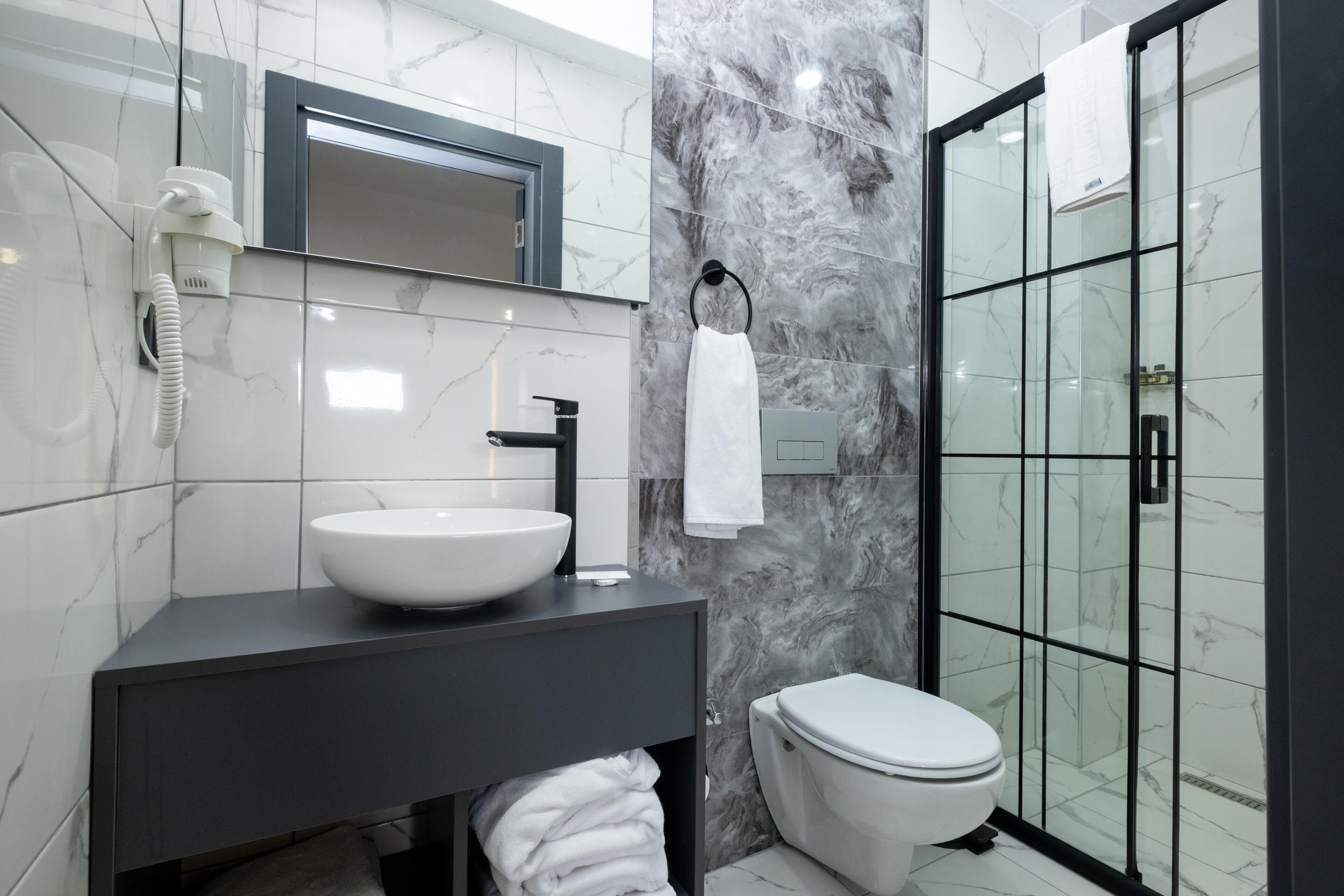 Ein modernes Badezimmer mit einem weißen Waschbecken, einer schwarzen Kommode und einer Duschkabine.