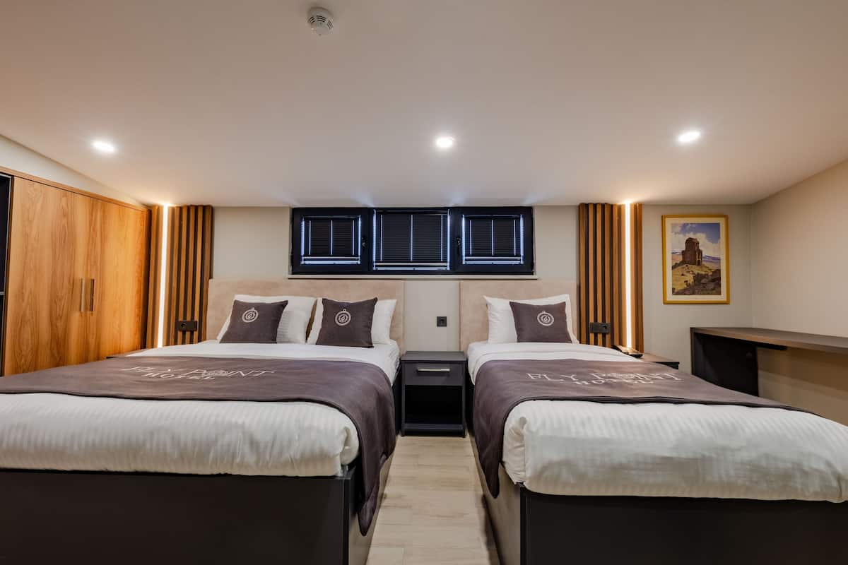 A modern hotel room with two beds, wooden wardrobe, a small desk, and a window with blinds.