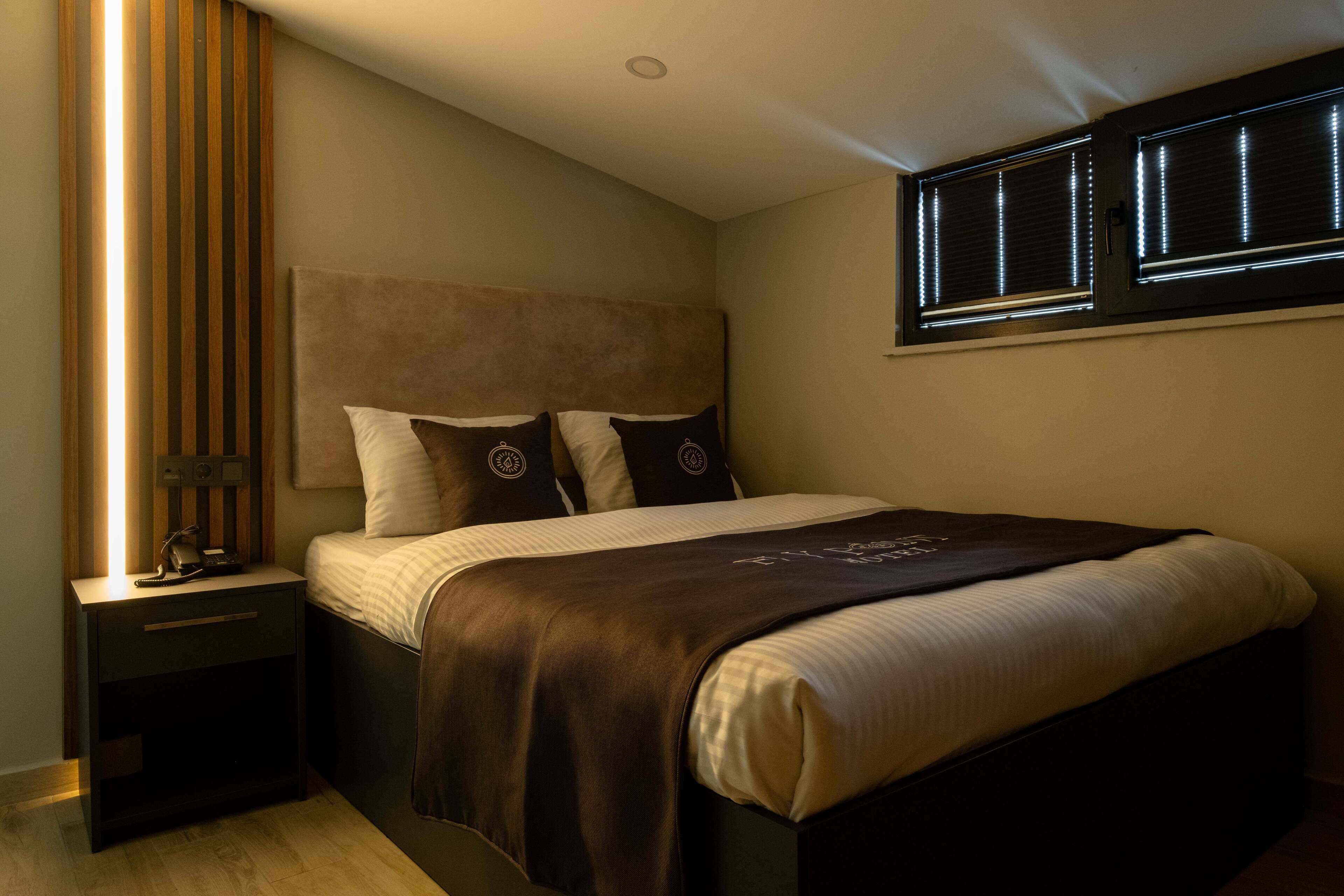 A bedroom with a bed, nightstands, a window with blinds, and a wooden panel on the wall.