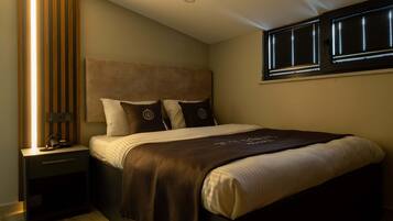 A bedroom with a bed, nightstands, a window with blinds, and a wooden panel on the wall.