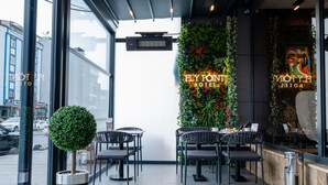 Un área de estar interior con mesas y sillas, una pared decorativa con plantas, y un letrero de neón para Fly Pont Hotel.
