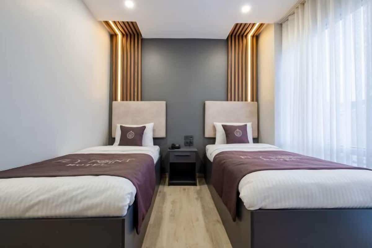 A hotel room with two beds, a nightstand, and a window with curtains.