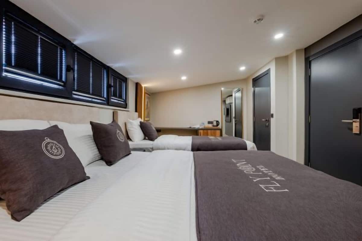 A hotel room with a large bed, a desk, a wardrobe, and a window with blinds.