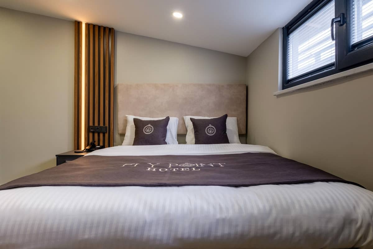 A hotel room with a bed, a nightstand, a headboard, and a window with blinds.