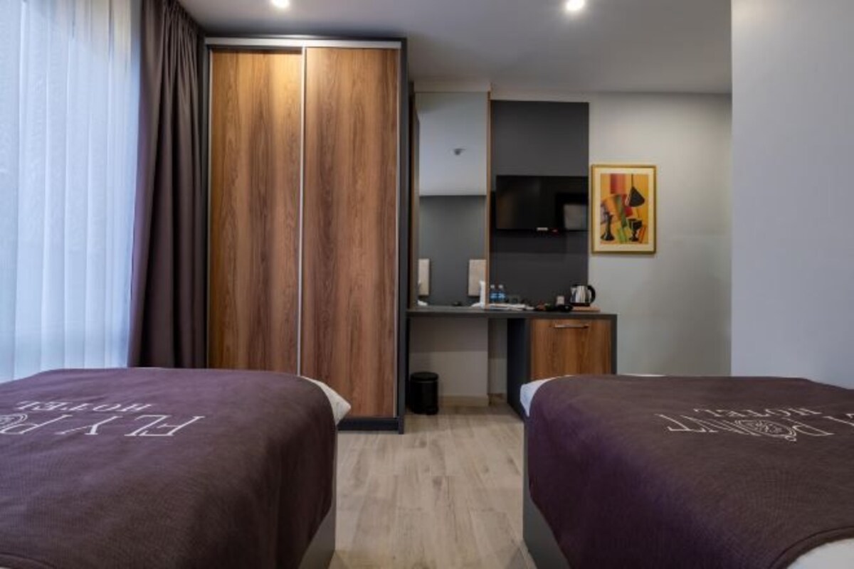 Une chambre d’hôtel avec deux lits, une armoire, un bureau avec une chaise, une télévision et un tableau au mur.