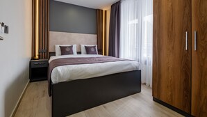 Un dormitorio moderno con una cama grande, un armario de madera y una mesita de noche con lámpara.