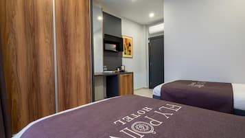 A hotel room with two beds, a desk, a wardrobe, and a television on the wall.