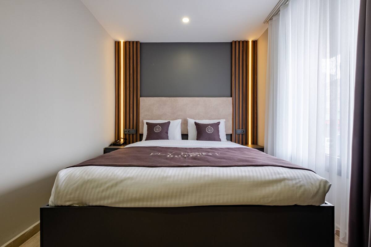 A modern hotel room with a large bed, a dark headboard, and a neutral color scheme.