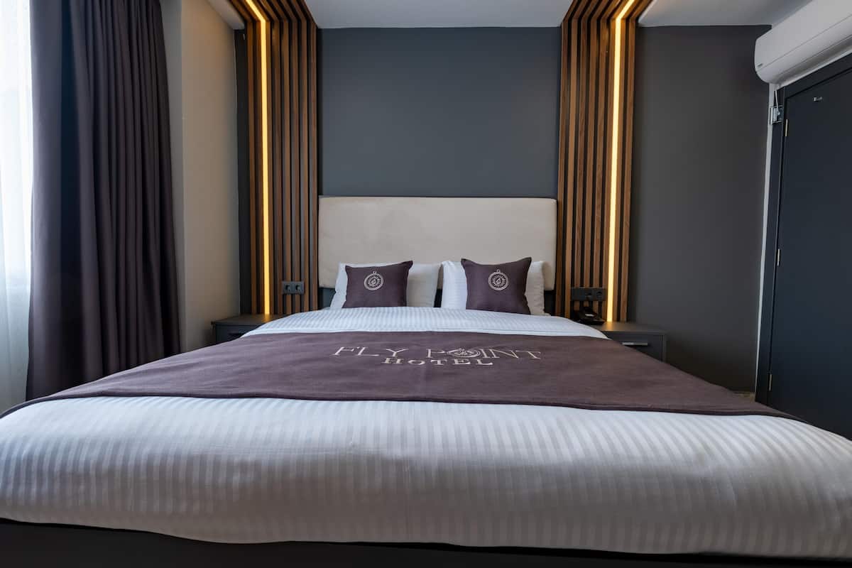 A neatly made bed with a headboard, two pillows, and a blanket with the hotel name.