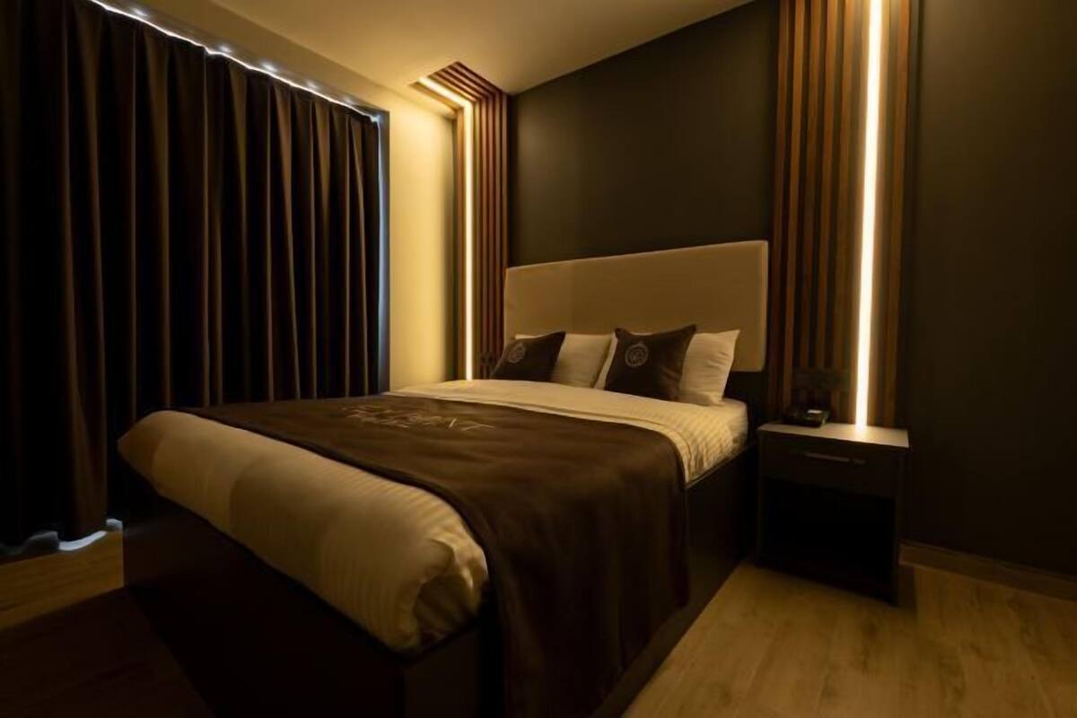 A modern bedroom with a large bed, a nightstand, and a wall-mounted light fixture.