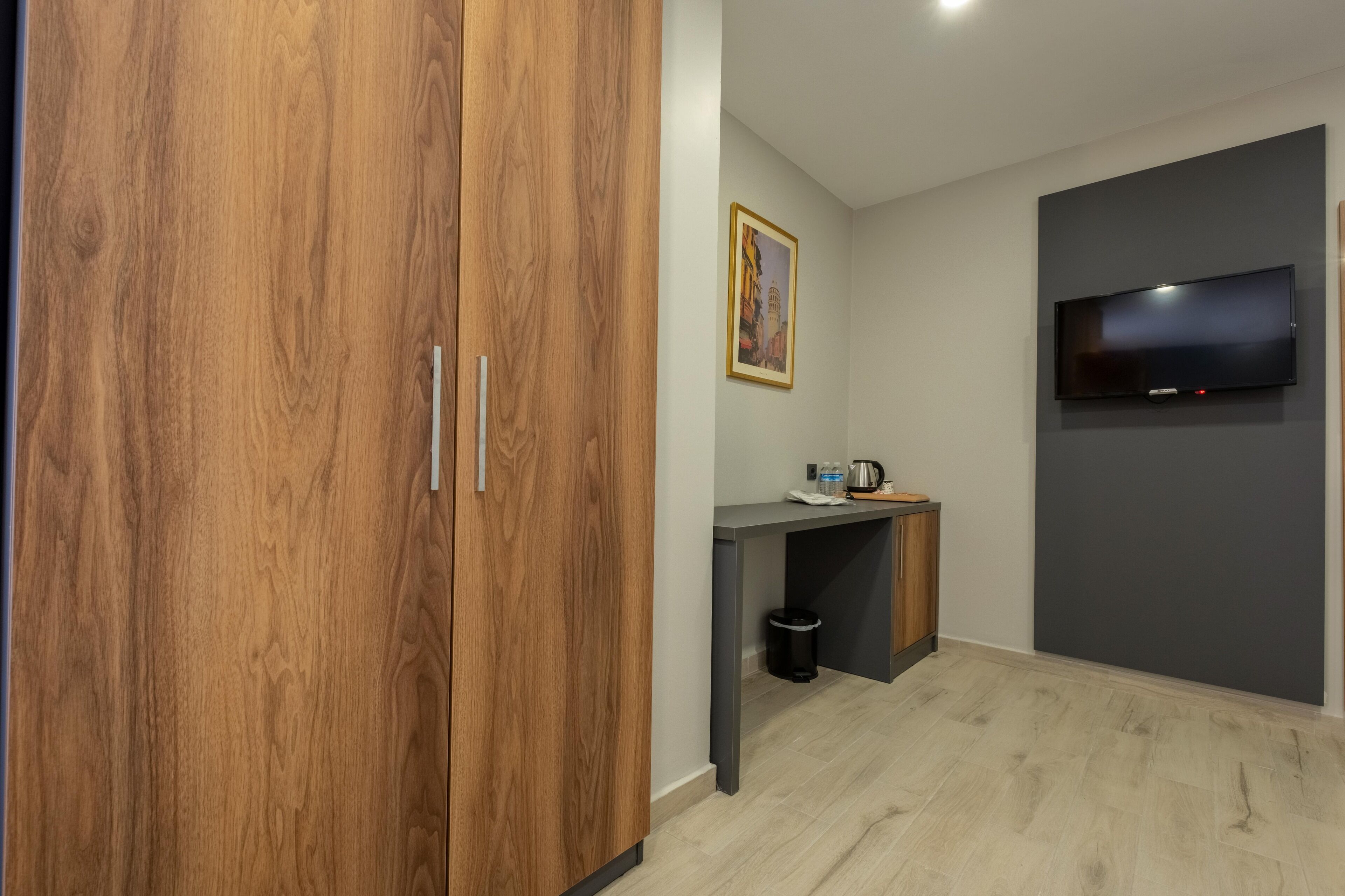 A modern room with a wooden wardrobe, a small desk with a kettle, and a flat-screen TV mounted on the wall.