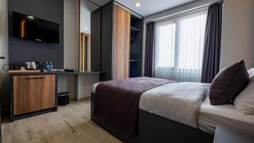 Ein modernes Hotelzimmer mit einem Bett, einem Schreibtisch mit Wasserkocher, einem Flachbildfernseher und einem großen Spiegel.