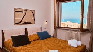 Une chambre d’hôtel avec un lit, des oreillers, une fenêtre donnant sur un paysage agréable et une œuvre d’art accrochée au mur.