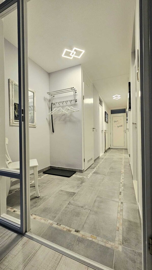 Un couloir avec un sol carrelé, un porte-manteau, un banc et une porte sur laquelle est apposée une pancarte.