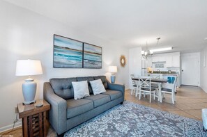 A living room with a grey sofa, two lamps, a patterned rug, and a kitchen in the background. - Family friendly, great amenities on the beach (Gulf Shores)