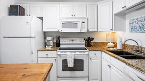 Una cocina con armarios blancos, un refrigerador blanco, un microondas, una estufa y un lavamanos.