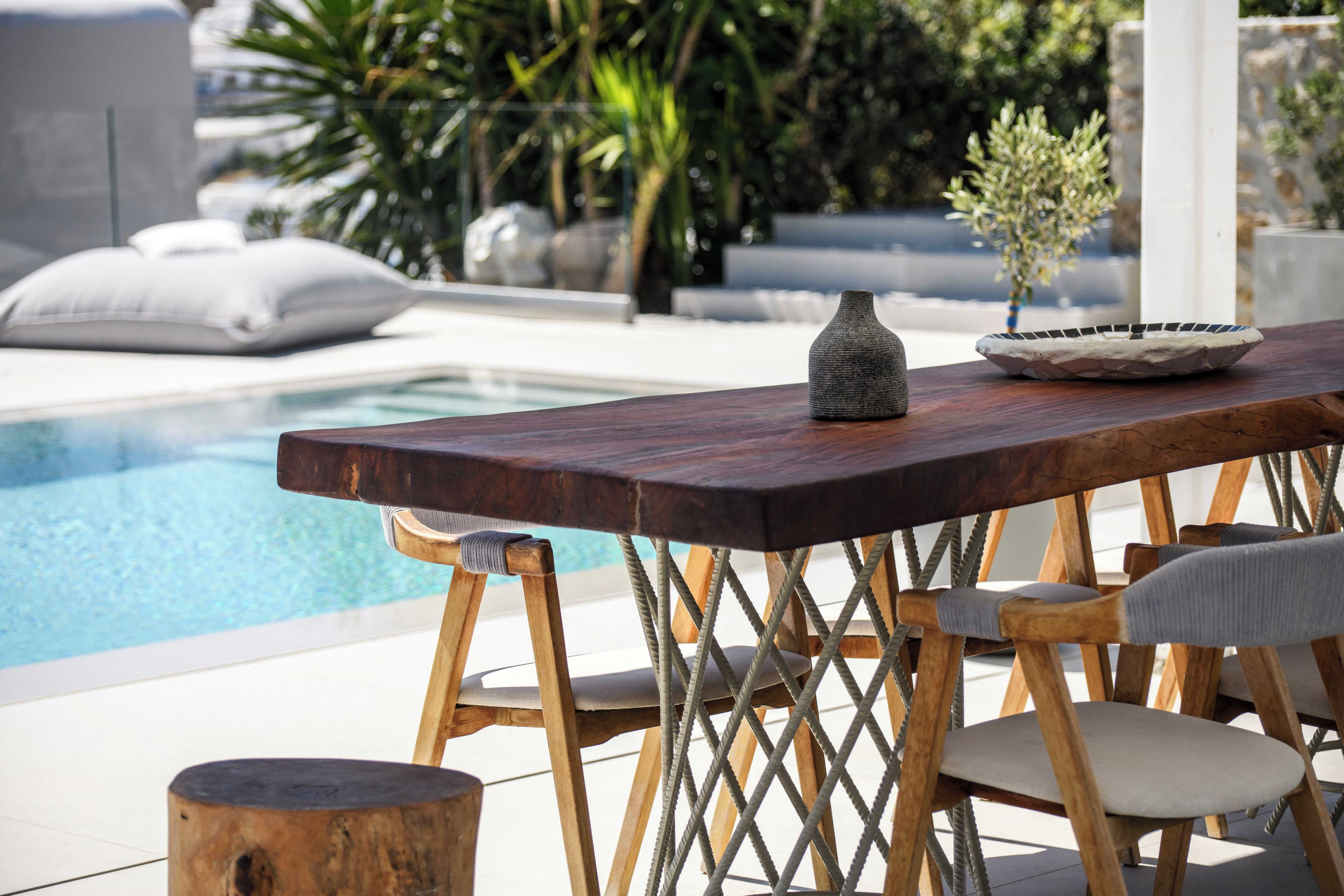 A poolside area with a wooden table, two chairs, and a decorative bowl.
