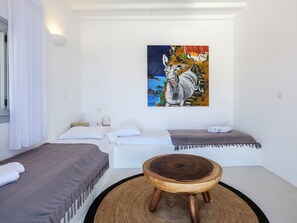 Una habitación con dos camas, un taburete de madera y un cuadro en la pared.