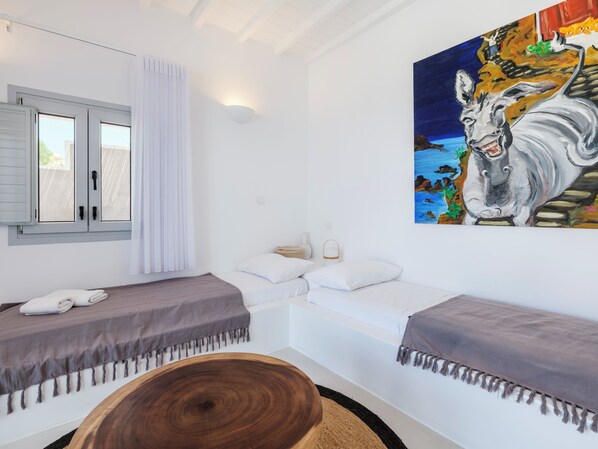 Una habitación con dos camas, un cuadro, una ventana con cortinas y una mesa de madera.