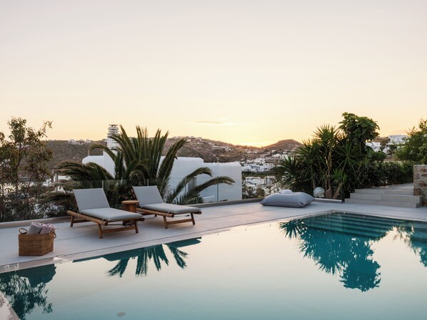 Un espace aménagé au bord de la piscine, avec des chaises longues et une vue dégagée sur une ville située sur une colline.