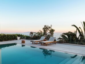 Una piscina con dos sillas de descanso y vista al mar.