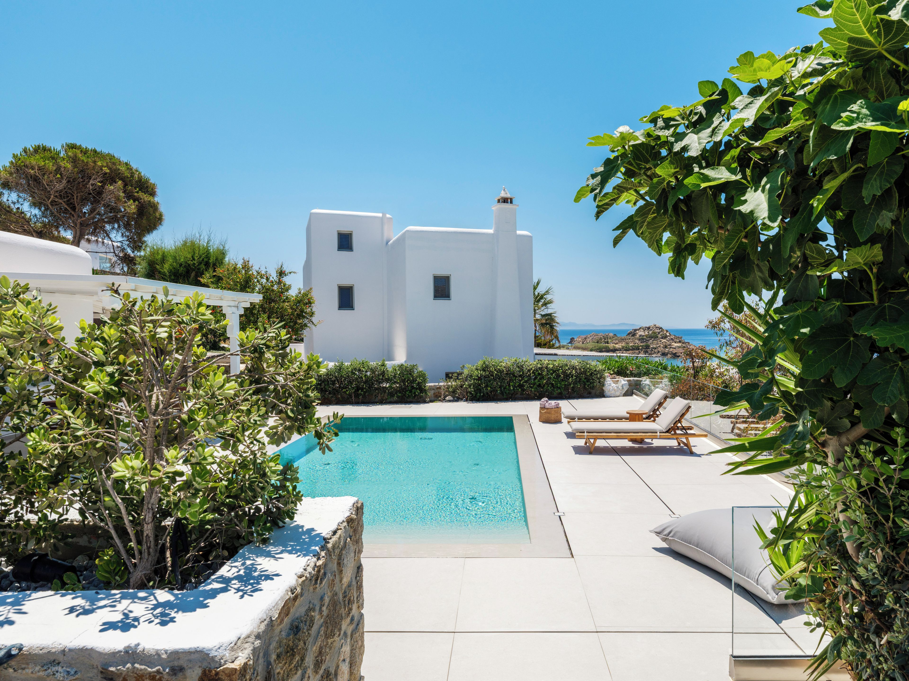 Un espace piscine offrant une vue sur la mer, avec des bâtiments blancs et une végétation luxuriante.