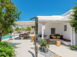 A covered outdoor seating area with a pool, stone walls, and a view of the landscape.