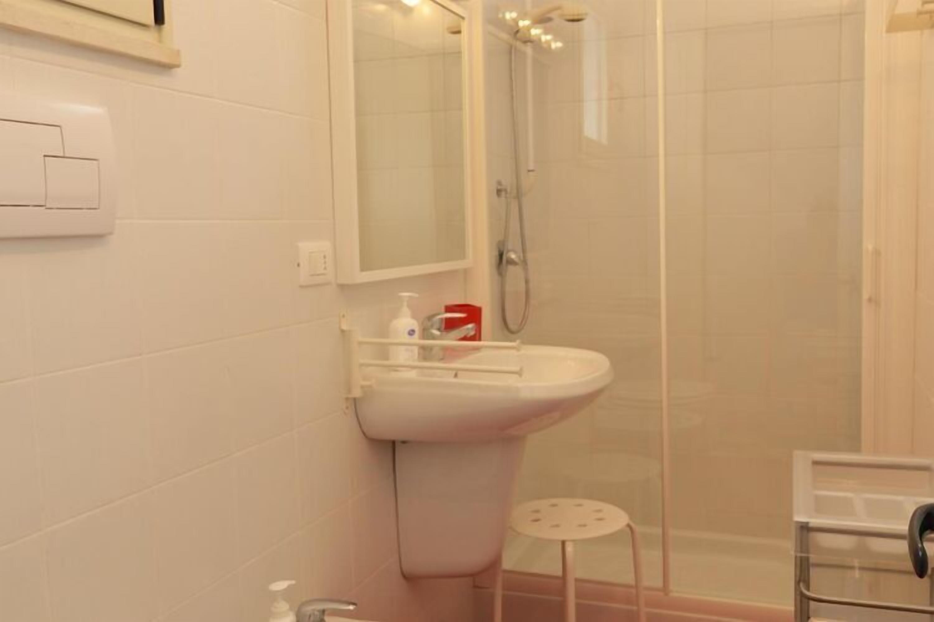 A bathroom with a sink, mirror, shower, and a small stool.