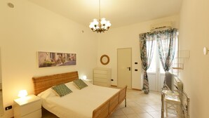 Une chambre à coucher comprenant un lit, une table de chevet, une lampe de chevet, des œuvres d’art mural, un miroir rond, une porte et une fenêtre avec des rideaux.